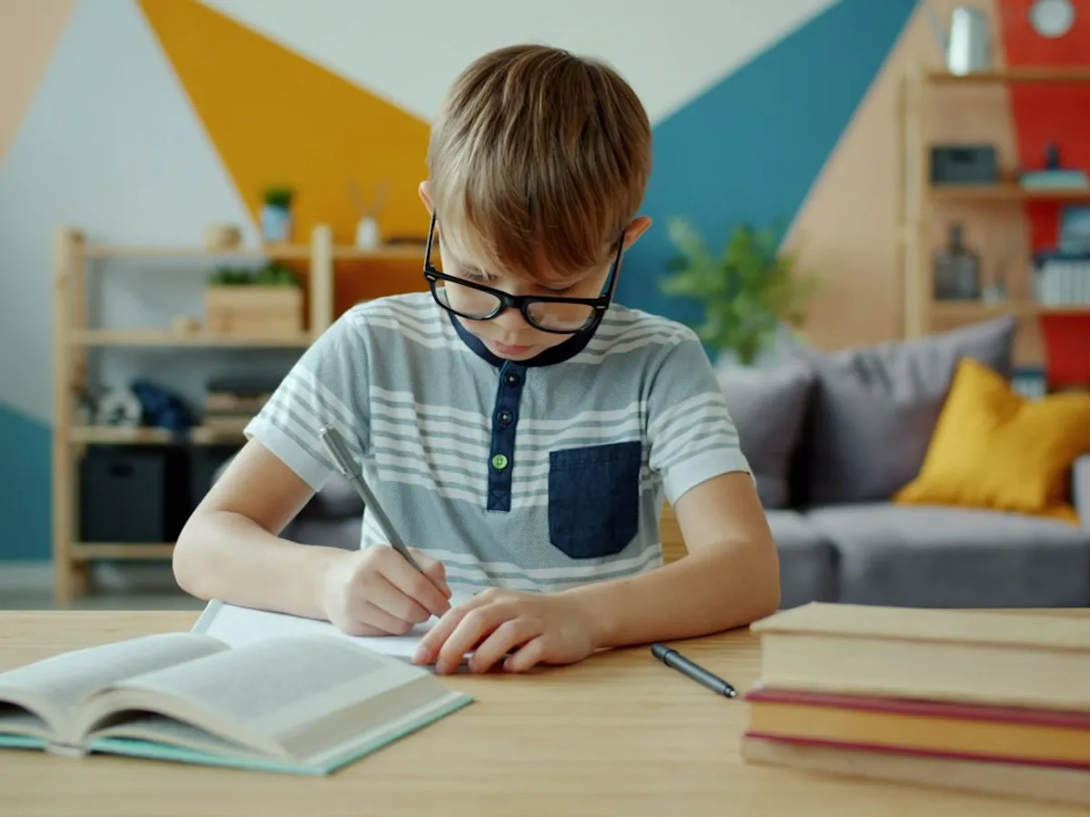 نوروفیدبک یا ریتالین؟ پسربچه‌ای با عینک در حال نوشتن در دفتر، تمرکز در درمان ADHD
